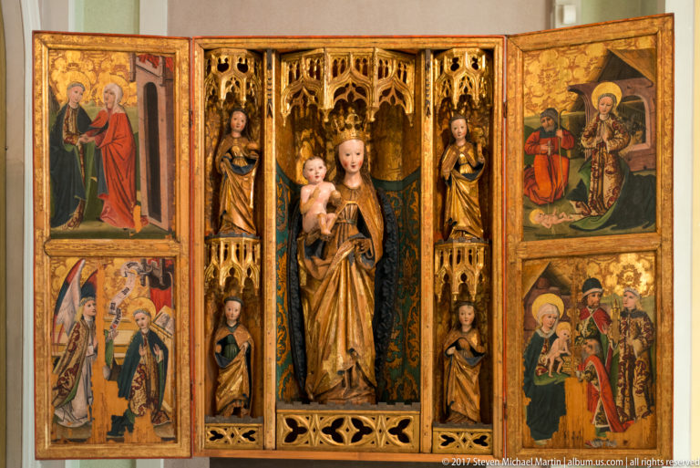 Late medieval winged altarpiece with the Virgin and Child, carved saints, gilded tracery, and painted side panels.