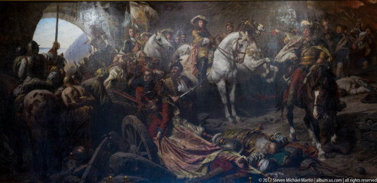 Large battle painting with mounted officers, a prominent white horse, fallen soldiers, and battlefield smoke.