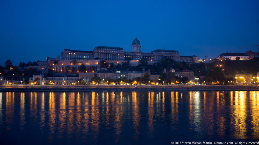 Buda Castle at blue hour, its illuminated palace dome and hillside buildings reflected in the Danube.