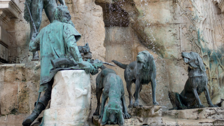 Bronze seated figure and hunting dogs against the rocky cascade of the Matthias Fountain at Buda Castle.