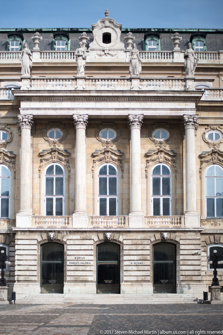 Frontal palace façade with giant columns, arched windows, oval openings, and balustrades at the Hungarian National Gallery.