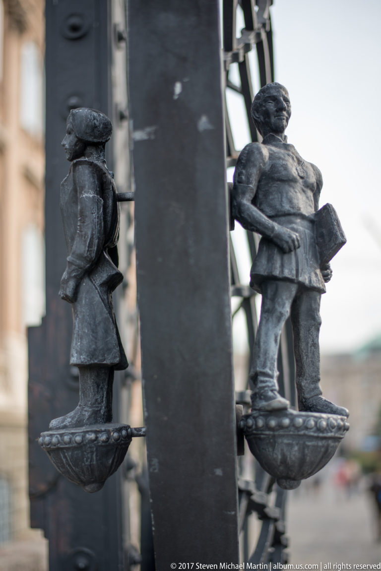Two small cast-metal soldier figures mounted on separate brackets of a black iron gate.