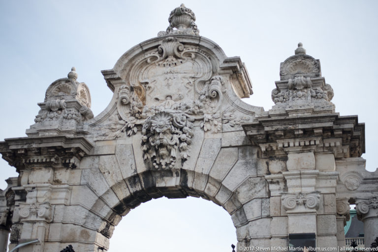 Ornate stone arch crowned by a cartouche, garlands, scrolls, and decorative finials at Buda Castle.