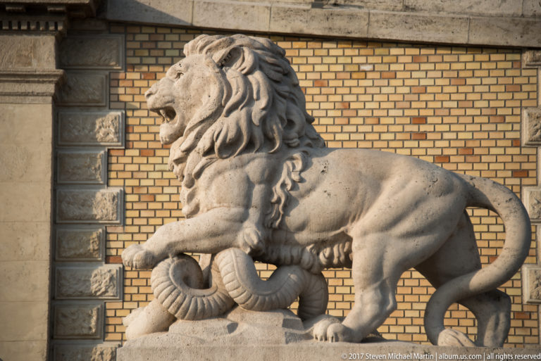 Profile view of a carved stone lion beside a yellow-brick wall at the Castle Garden Bazaar.