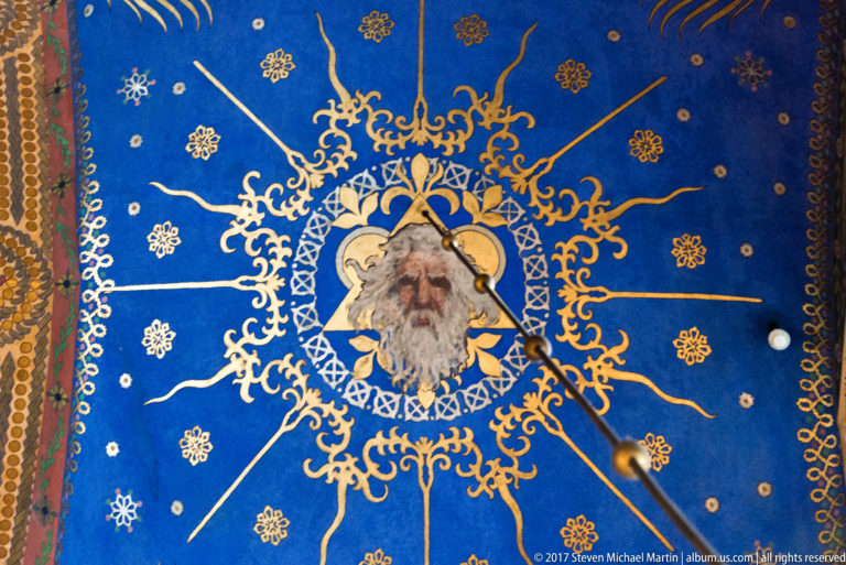 Bearded sacred figure in a circular painted medallion, surrounded by gold tracery, stars, and floral motifs on deep blue.