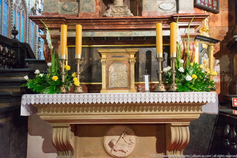 Small side altar with white cloth, tall yellow candles, flowers, greenery, and a central tabernacle-like structure.