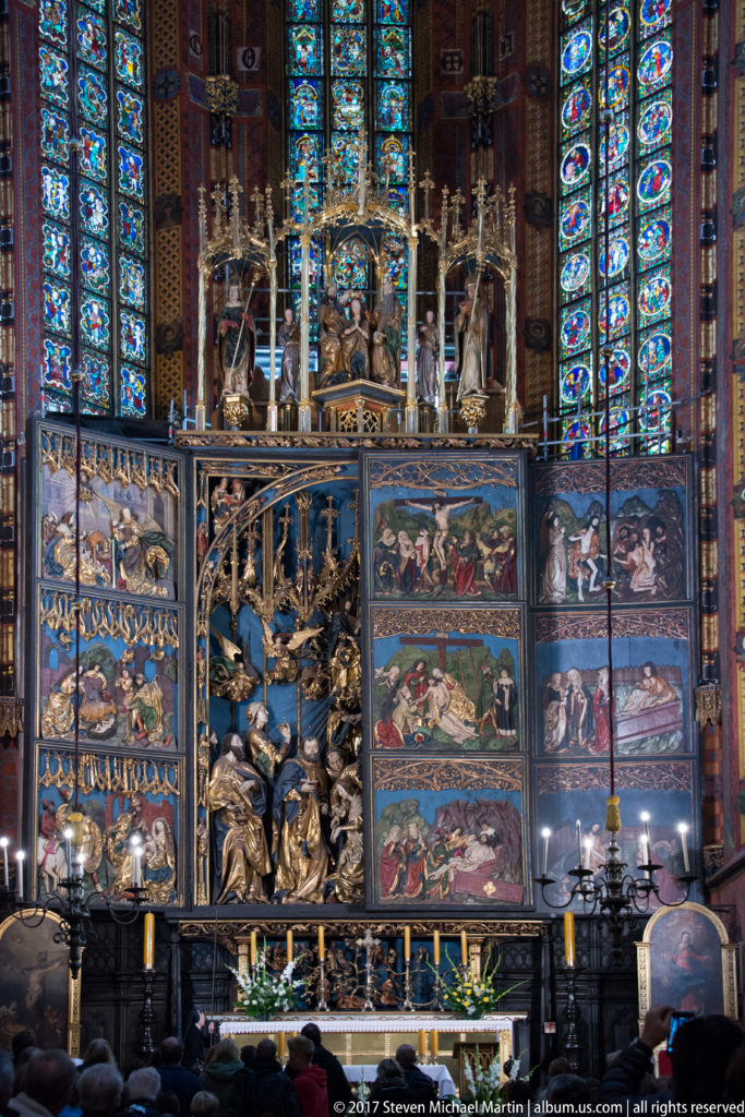 Frontal view of the open Veit Stoss Altarpiece beneath tall stained-glass windows, with carved central figures and narrative wings.