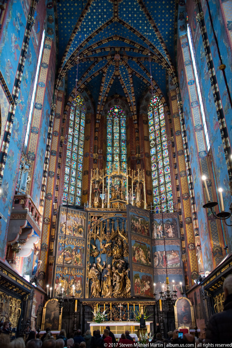 Wide chancel view with the Veit Stoss Altarpiece beneath tall stained glass and blue star-patterned Gothic vaulting.