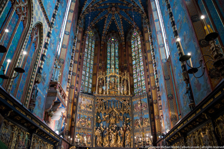 Vertical chancel view centered on the Veit Stoss Altarpiece beneath stained-glass lancets and blue star-patterned rib vaulting.