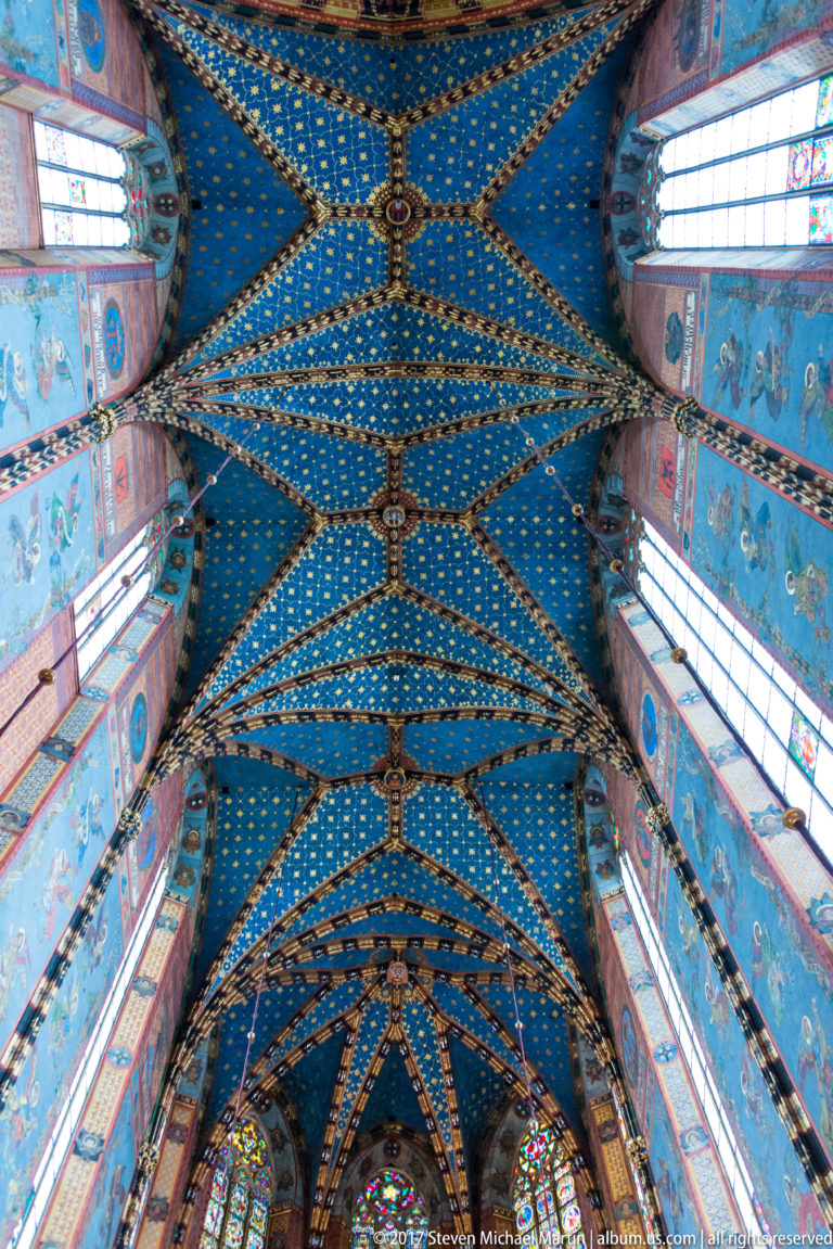 Long upward view of blue star-patterned nave vaulting with repeating ribs, bosses, painted upper walls, and clerestory windows.