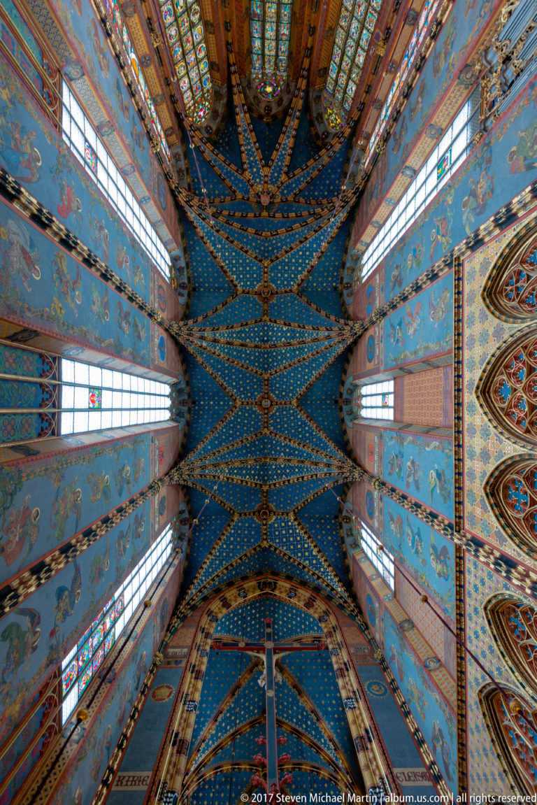 Upward axial view of blue star-patterned rib vaulting, clerestory windows, and painted upper walls inside St. Mary’s Basilica.