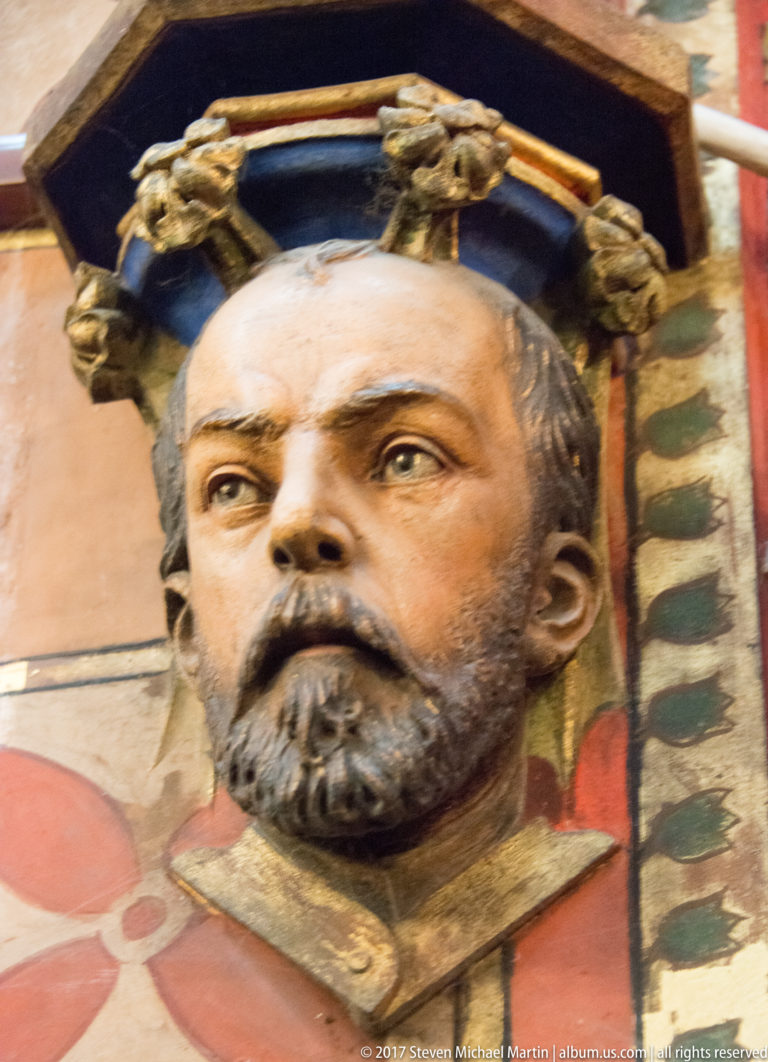 Close view of a polychrome bearded male head projecting from painted architectural decoration inside the basilica.