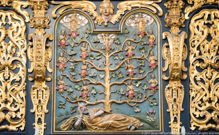 Ornate relief with a reclining male figure beneath a branching tree filled with small figures, flowers, and gilded decoration.