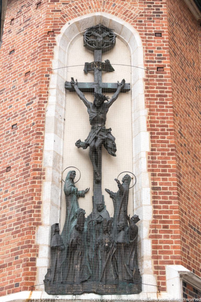 Crucifixion group with Christ on the cross and mourners below, set within a tall pointed-arch recess in the red-brick exterior.