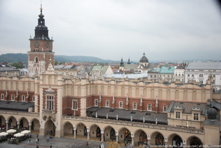 Closer elevated view of Town Hall Tower above the Cloth Hall roofline, with historic rooftops and church domes beyond.