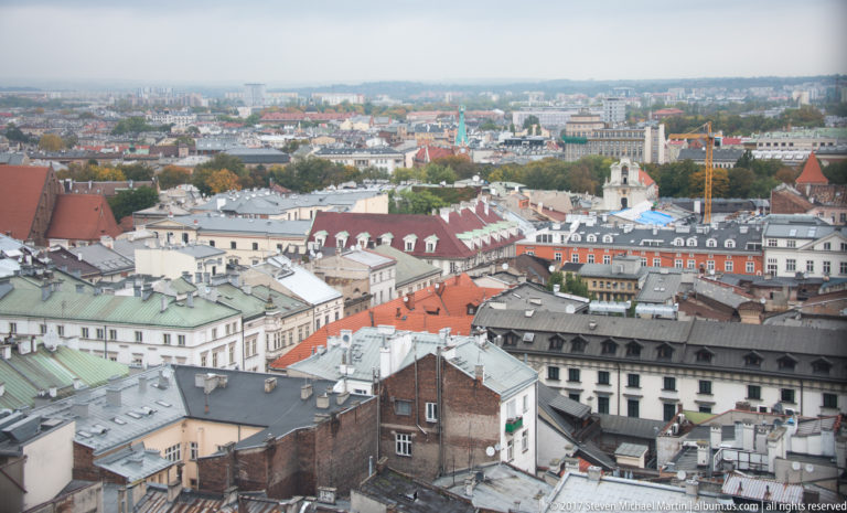 Elevated panorama across Krakow’s historic center with red, gray, and green roofs, church towers, and dense urban blocks.