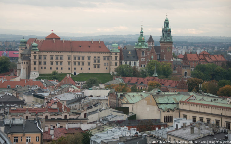 Elevated telephoto view toward Wawel Hill, showing the castle complex and cathedral towers beyond Krakow’s rooftops.