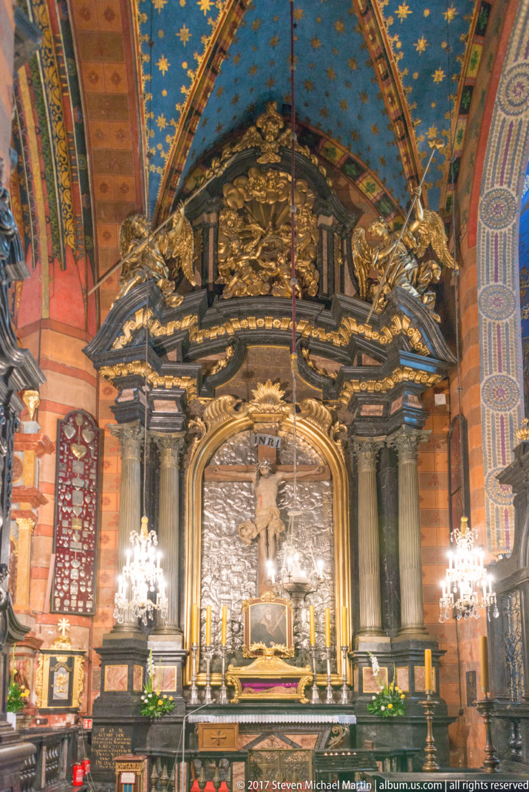 Ornate interior altar with gilded sculpture, candles, chandeliers, and richly painted walls beneath a decorated vault.