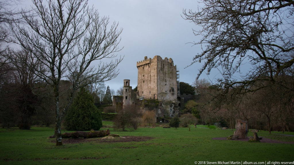 Blarney Castle keep seen across a broad lawn framed by leafless trees and landscaped shrubs.