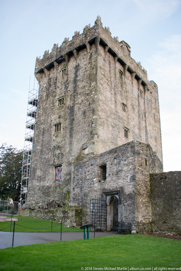 Close exterior of Blarney Castle keep showing rough stone walls, small openings, corbels, doorway, railings, and scaffolding.