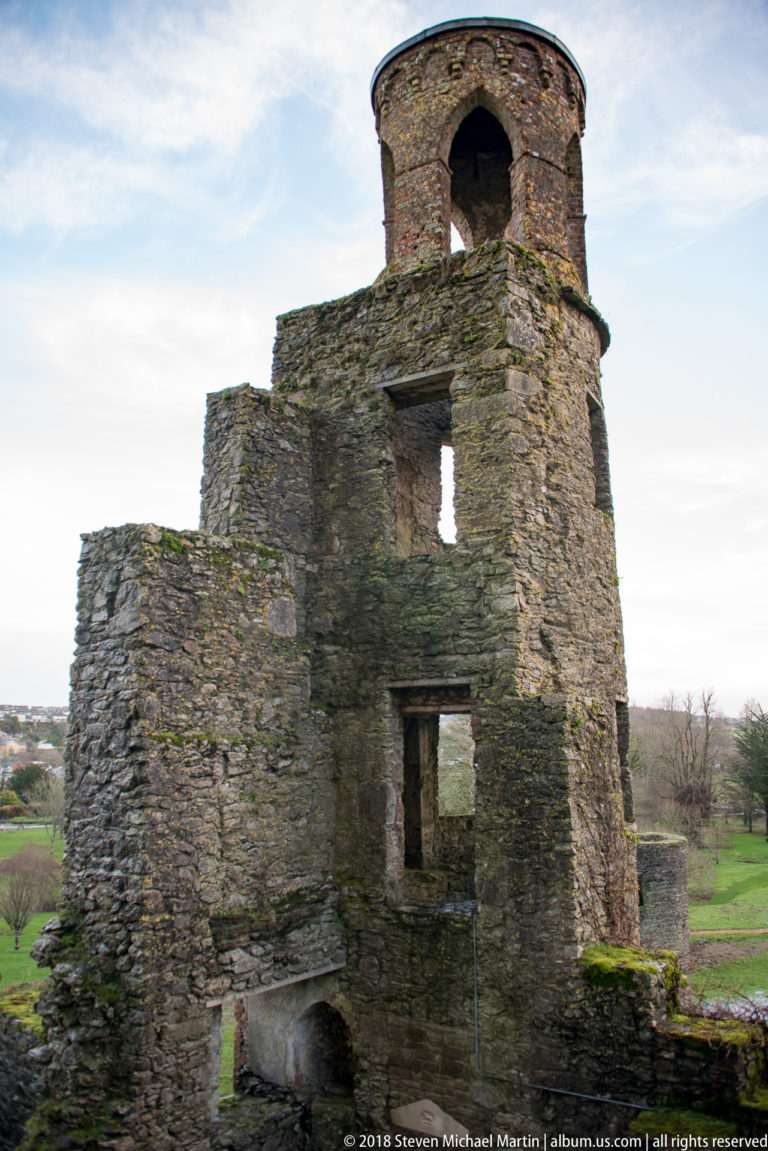 Roofless stone tower with a large arched upper opening, smaller window apertures, and adjoining ruined walls.