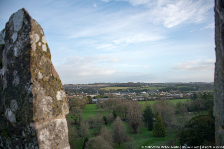 Green countryside and estate grounds seen through a narrow stone opening in Blarney Castle.