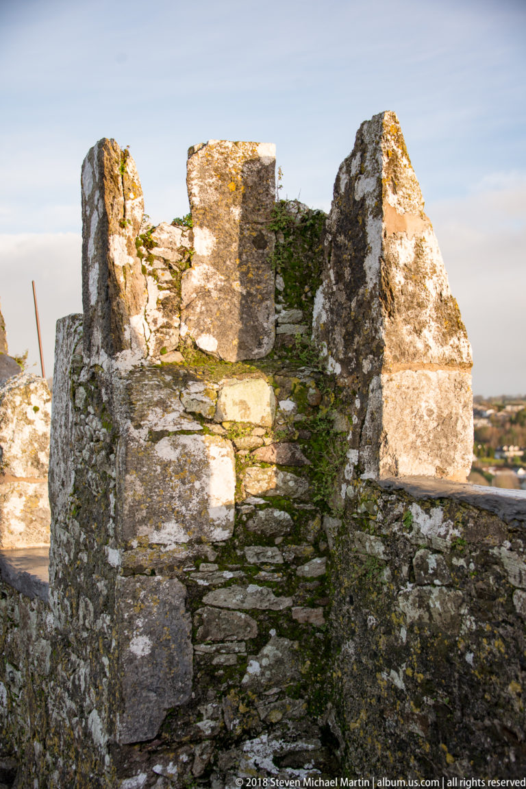Close detail of weathered stone crenellations with moss, lichen, and irregular rubble along the castle parapet.