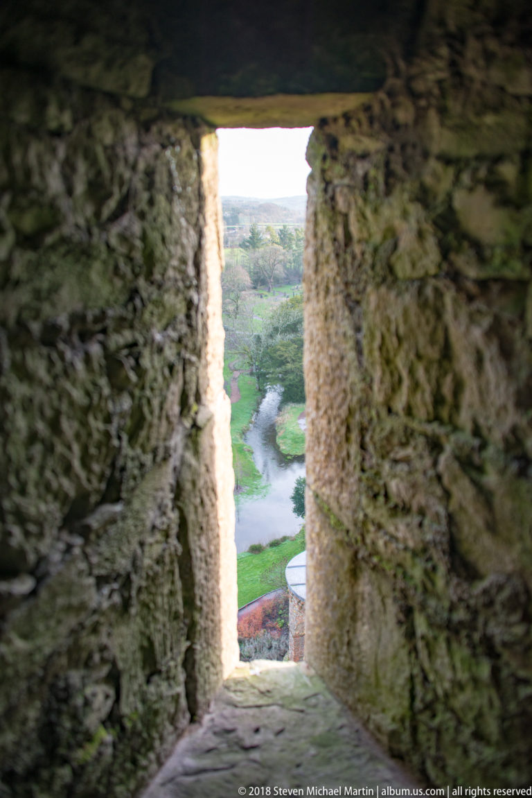 River or stream and green gardens seen through a deep narrow stone opening in Blarney Castle.