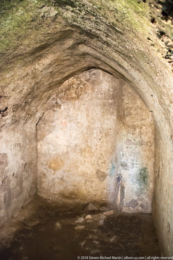 Low barrel-vaulted stone chamber with worn plaster, rough masonry walls, and a bare floor inside the castle.