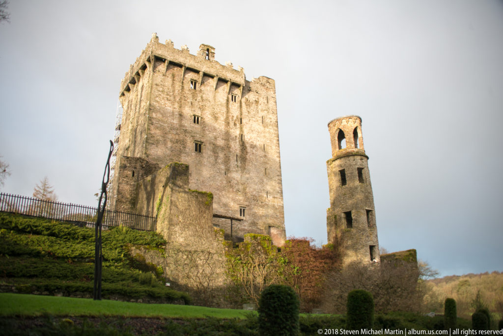 Blarney Castle keep and a narrower stone tower rising above terraced lawns and clipped shrubs.