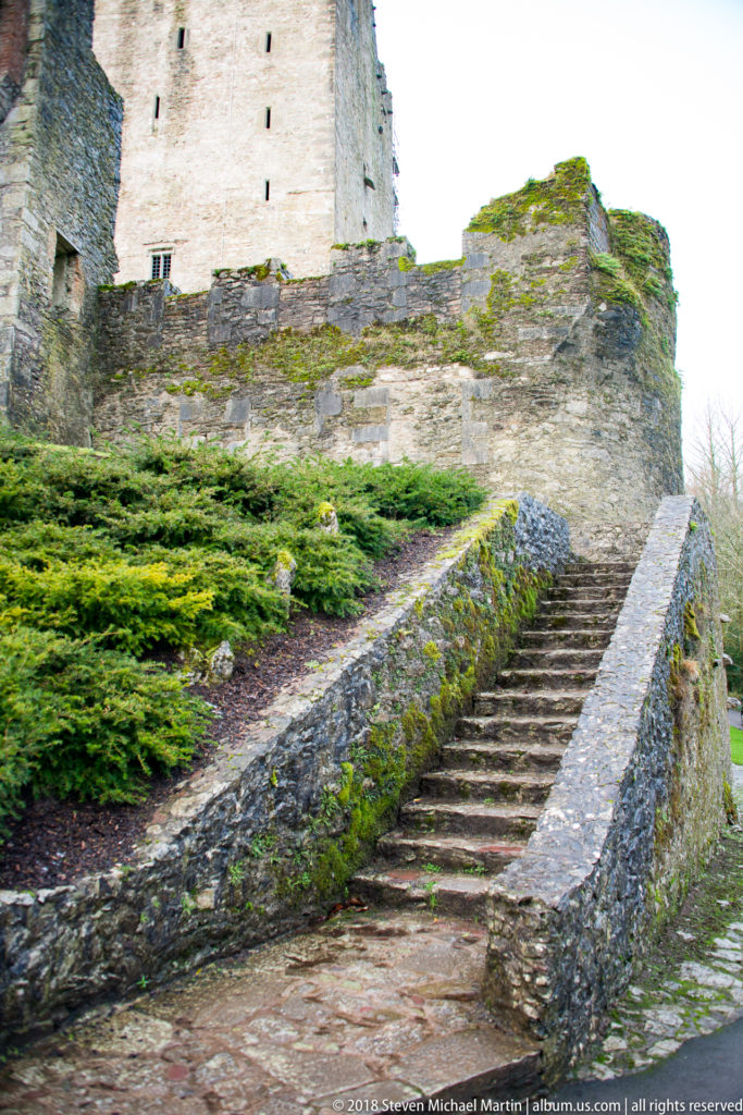 Stone steps and low walls ascending a landscaped slope toward part of Blarney Castle.