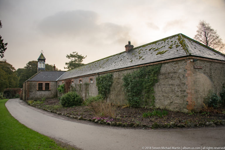 Long stone estate building with slate roof, small cupola, ivy, and a path curving alongside.