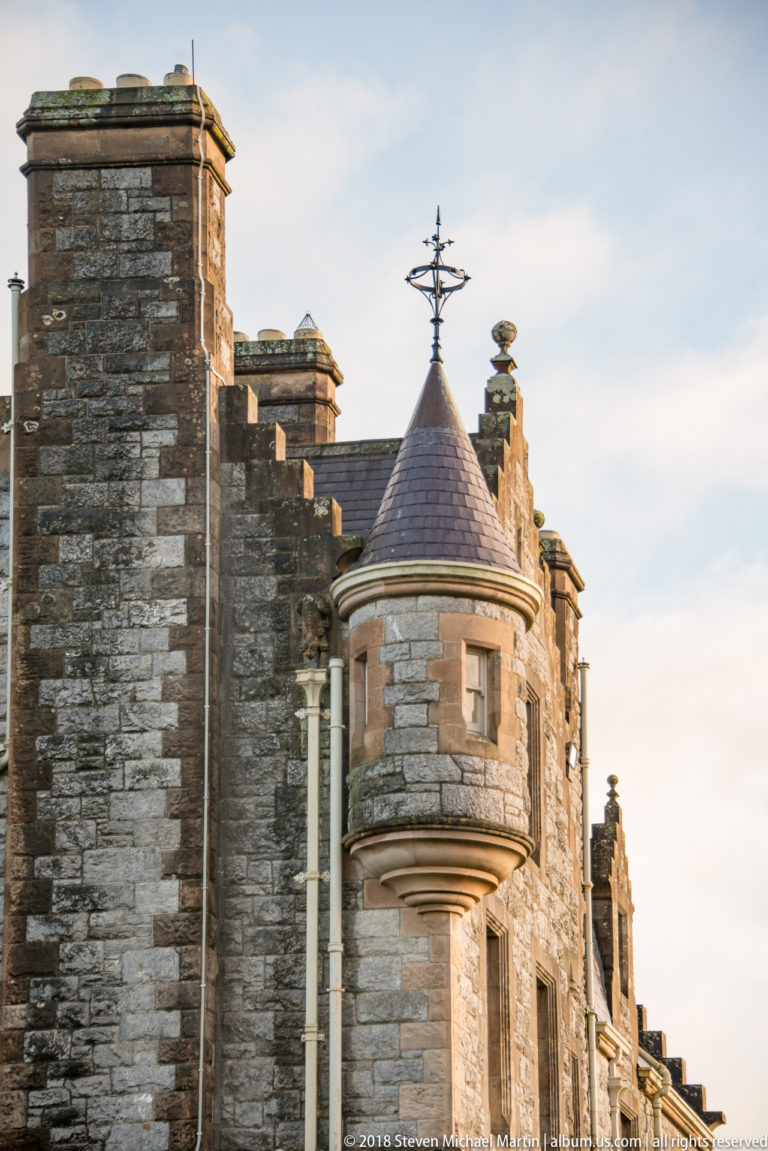 Round stone turret on Blarney House with conical slate roof, narrow windows, and decorative weather vane.