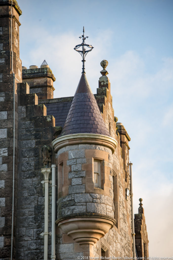 Close view of Blarney House turret with corbelled base, narrow windows, conical roof, and metal finial.