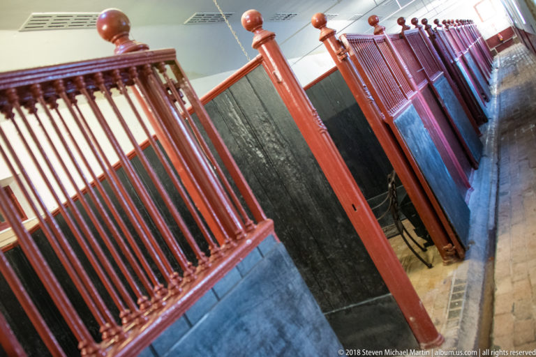 Row of red-painted wooden stall partitions with dark panels inside a paved estate service interior.
