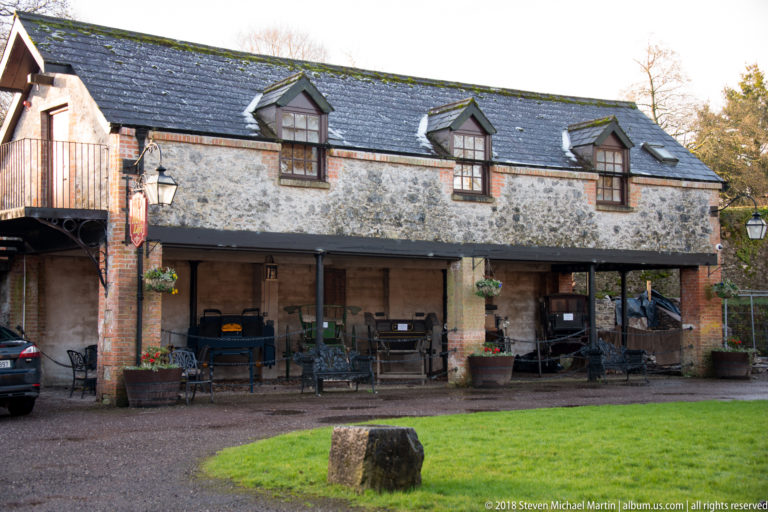 Stone two-story estate building with dormer windows, slate roof, and tables under a covered ground floor.