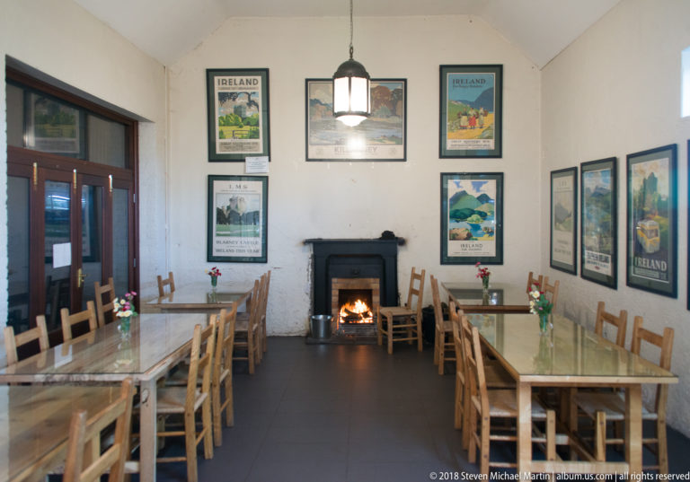 Dining room with wooden tables, chairs, a lit fireplace, pendant light, and framed Ireland travel posters.