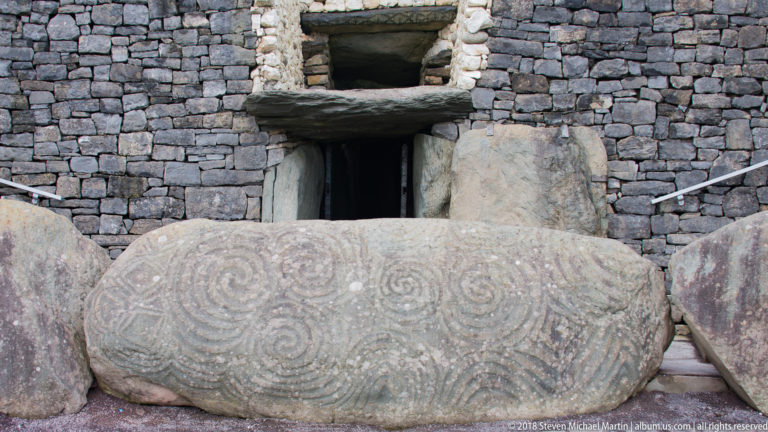Large carved Newgrange entrance stone covered with spirals, with the passage doorway behind it.