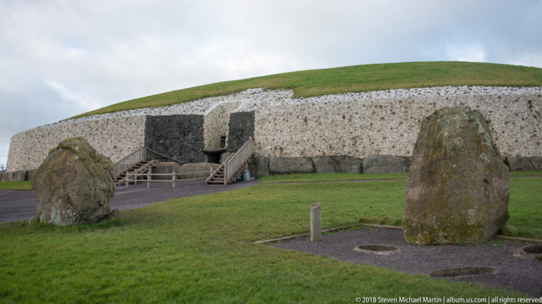 Newgrange mound and entrance behind two large standing stones on a grassy lawn.