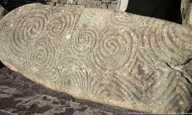 Oblique close-up of Newgrange entrance stone with spirals and geometric carvings beside the passage opening.