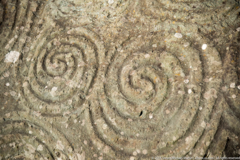 Tight close-up of two incised spiral motifs on a weathered megalithic stone.