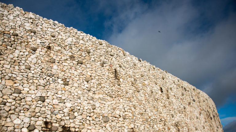 Low-angle view looking up along Newgrange’s curved quartz-and-cobble façade against dark sky.
