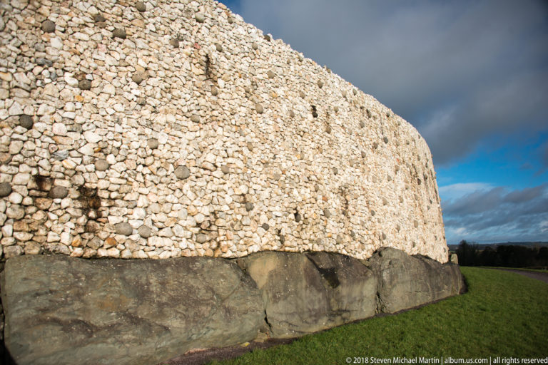 Large dark kerbstones forming the base of Newgrange beneath the pale quartz-and-cobble façade.