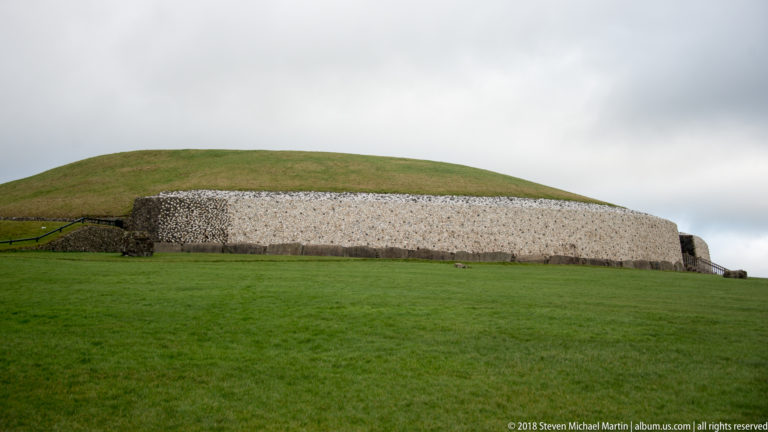 Long side view of Newgrange showing the grassy mound above its pale quartz-and-cobble façade.