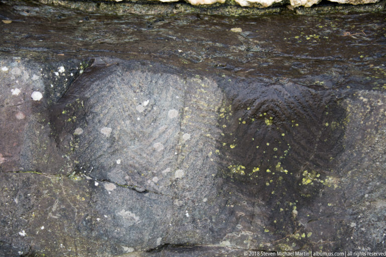 Faint incised geometric and chevron-like carvings on a dark weathered stone surface at Newgrange.