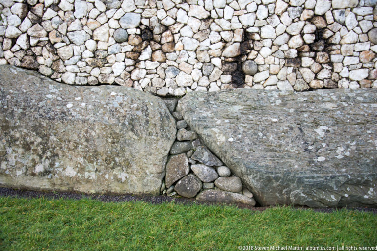 Close view of massive Newgrange base stones, small packing stones, and pale cobble revetment above.