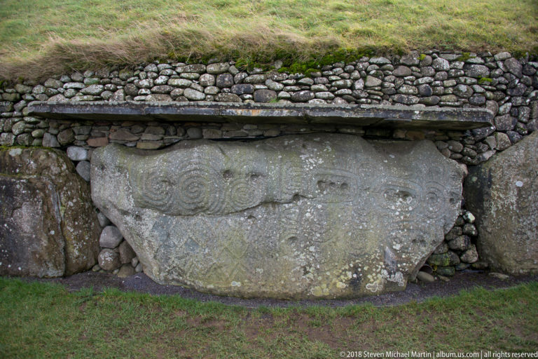 Massive carved stone beneath layered masonry, covered with spiral and curving incised designs across its weathered face.