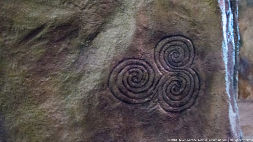 Three closely grouped spiral carvings forming a triangular motif on a dark megalithic stone surface.