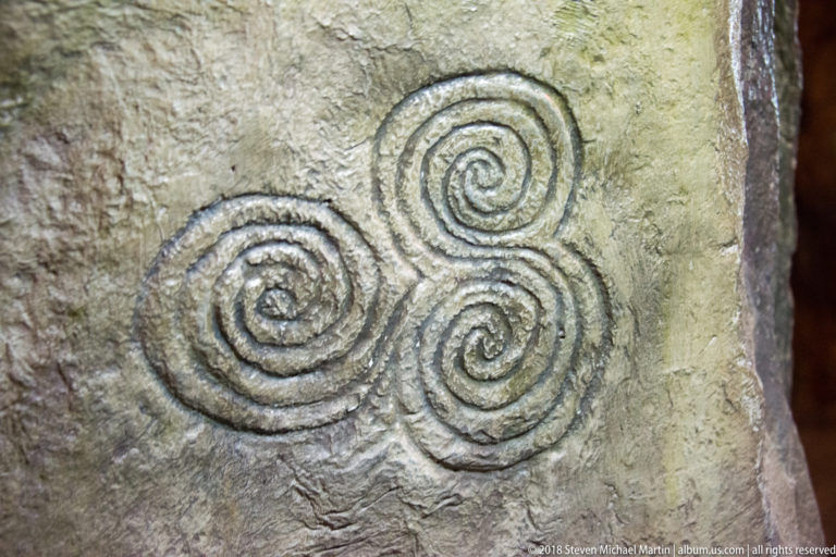 Three connected spiral motifs with clearly cut grooves on a pale, textured megalithic stone surface.