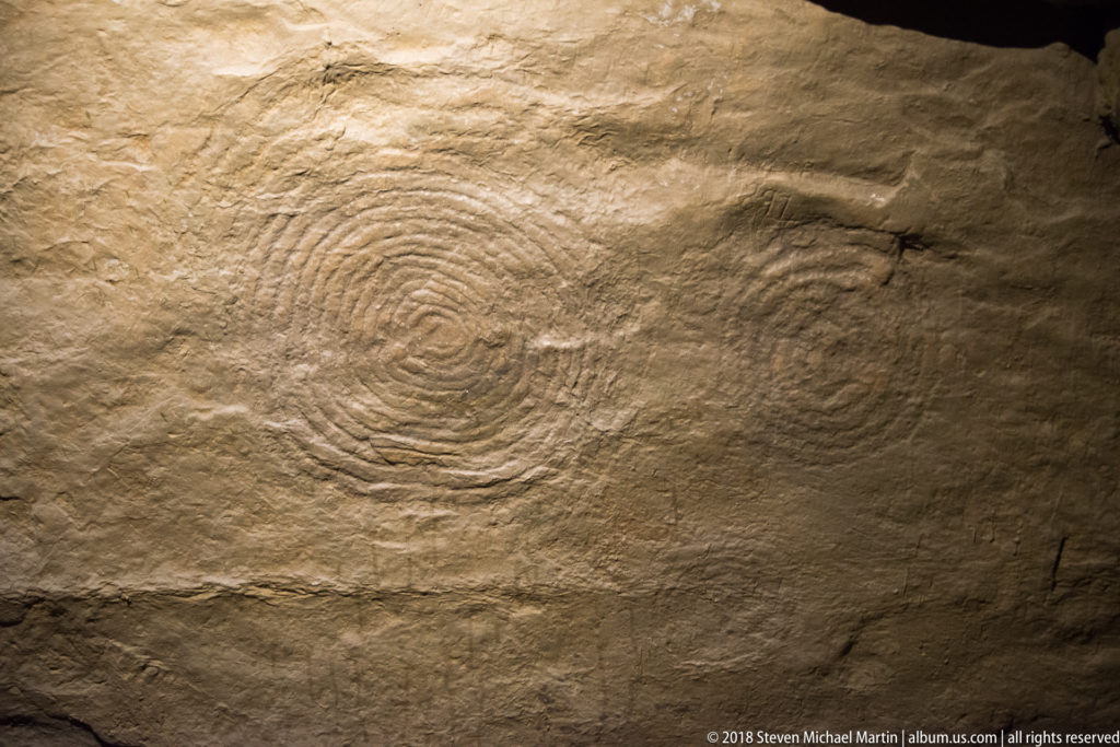 Broad stone surface with faint concentric curved carvings revealed by warm, oblique light.
